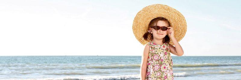 girl with sunglasses and giant floppy hat next to the beach